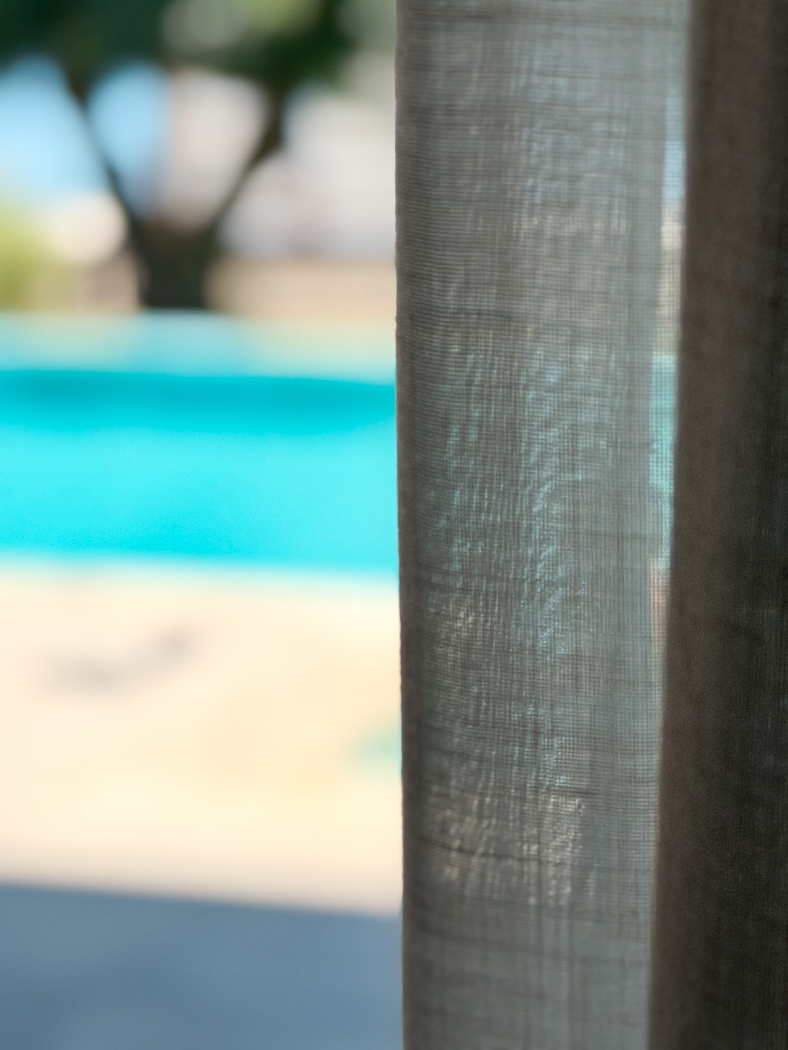 Close-up of a textured linen curtain with a soft-focus turquoise swimming pool in the background.