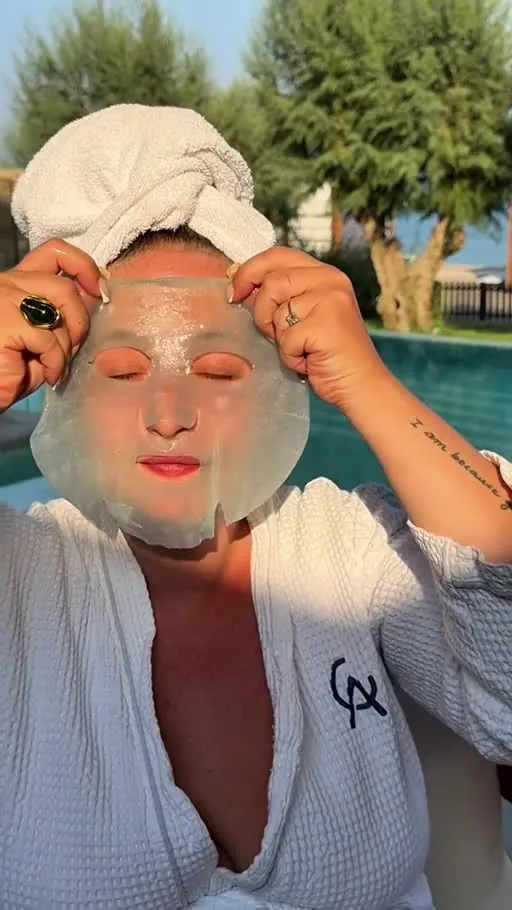 A translucent sheet mask being applied to skin in warm golden hour light, paired with a white waffle robe and towel.