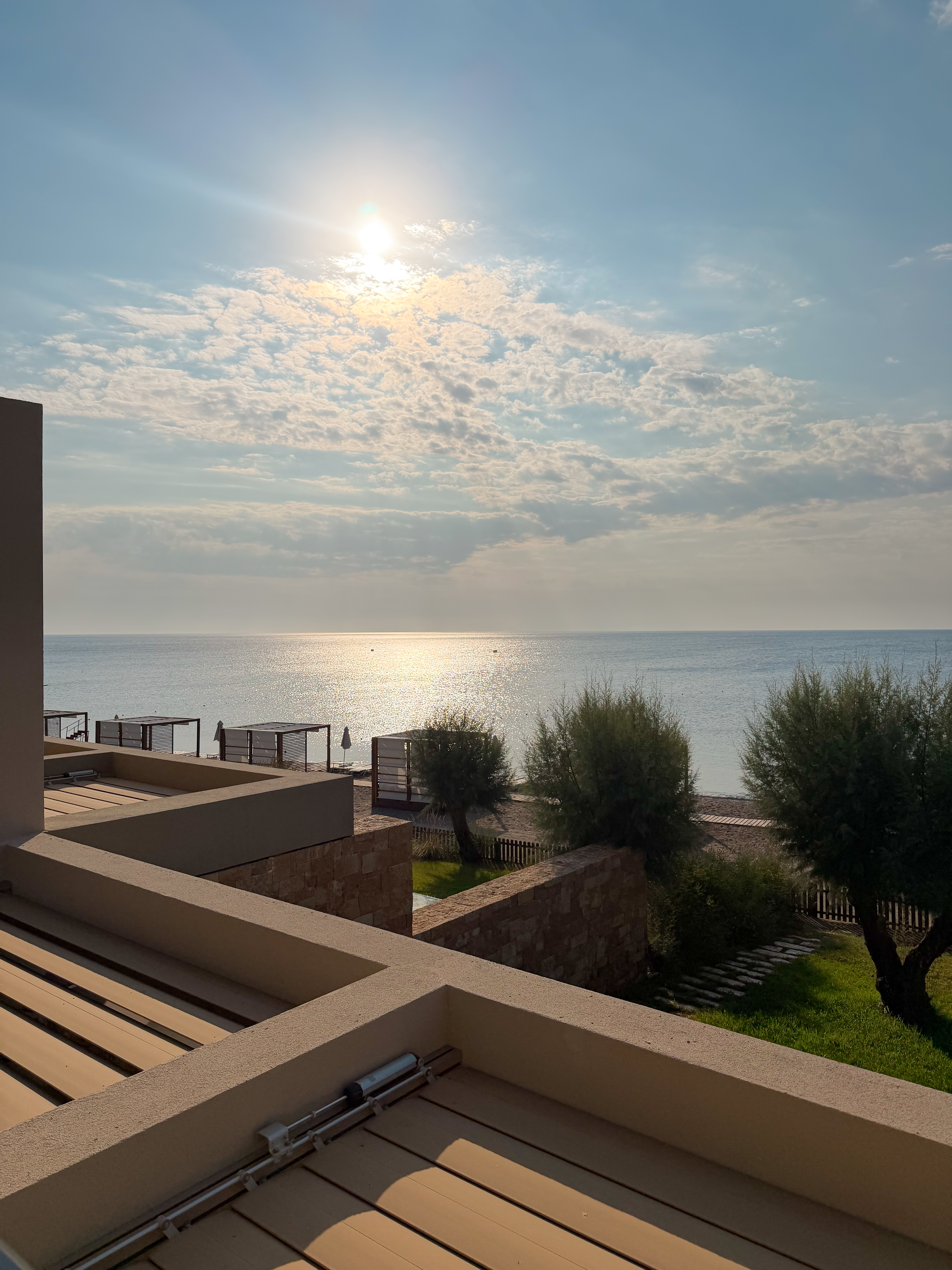 Modern stone terrace overlooking a quiet sea at sunrise, featuring soft morning light and coastal greenery.