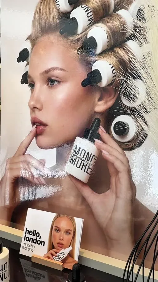 Close-up of a model display with hair wrapped around white dropper bottles like rollers in a warm, studio setting.