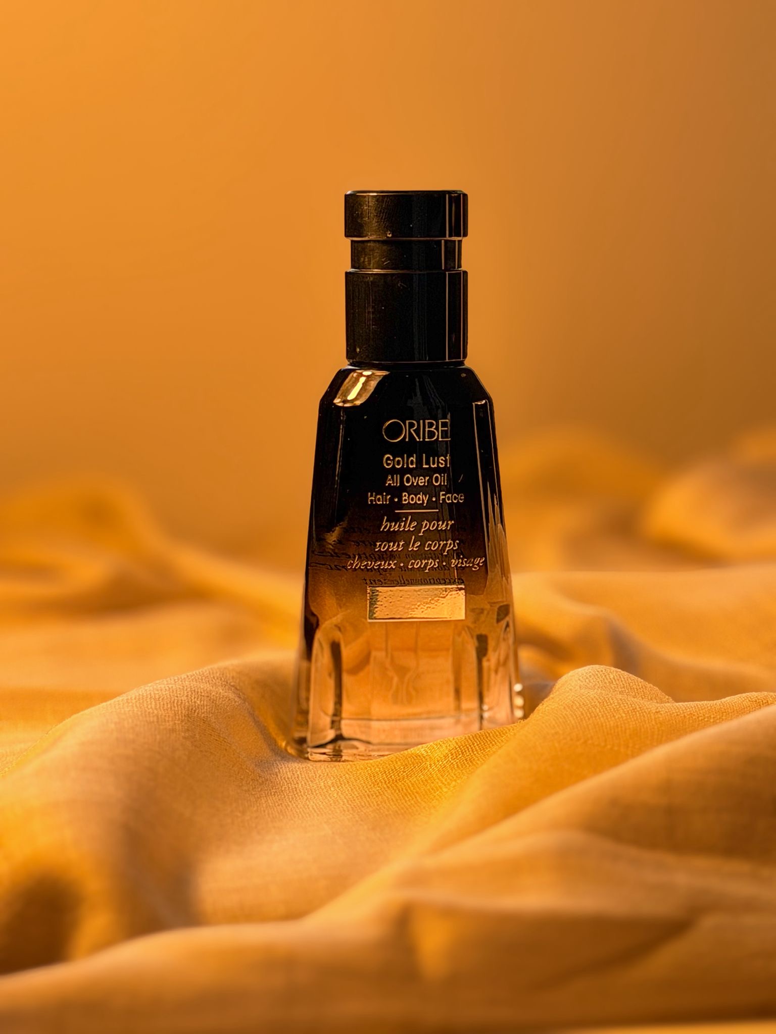 Oribe Gold Lust All Over Oil bottle styled on amber fabric for an editorial beauty ritual photo by Beauty With Ju