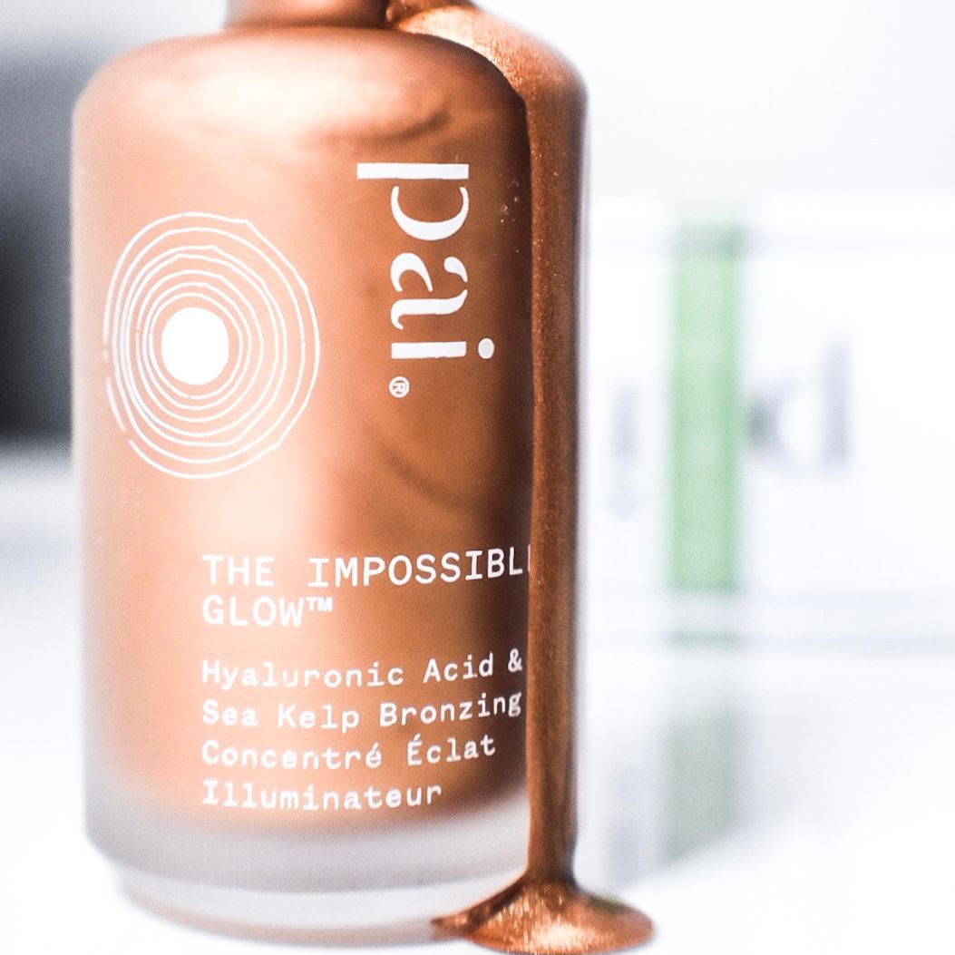 Close-up of a bronze liquid highlighter bottle with shimmering copper drops dripping down a frosted glass surface.